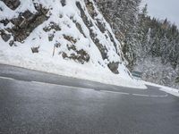 the road is very slippery and empty on a snowy day near a pine tree lined mountain