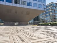 the empty square at a large office building with many windows and wooden floor tiles in front of it