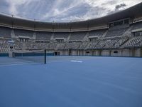 empty stadium with a tennis court and blue flooring and fans watching the game in view