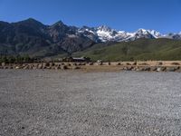 an empty stone field with snow capped mountains in the background on a clear day with a blue sky and some green bushes