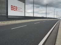 the empty street near an airport is surrounded by large billboards that read ber