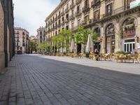 a empty street with benches, tables and umbrellas on either side of the walkway