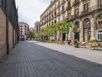 a empty street with benches, tables and umbrellas on either side of the walkway