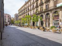 a empty street with benches, tables and umbrellas on either side of the walkway