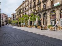 a empty street with benches, tables and umbrellas on either side of the walkway