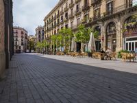 a empty street with benches, tables and umbrellas on either side of the walkway