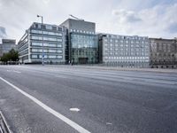 empty street with no people on it in front of a building with many windows and a bench by the side walk