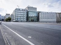 empty street with no people on it in front of a building with many windows and a bench by the side walk