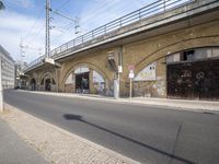 the empty street is next to a brick building and a bridge that has graffiti on it