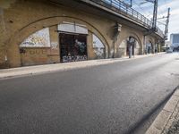 the empty street is next to a brick building and a bridge that has graffiti on it