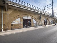the empty street is next to a brick building and a bridge that has graffiti on it