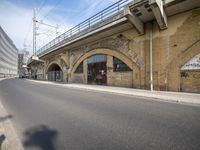 the empty street is next to a brick building and a bridge that has graffiti on it