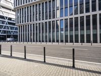 the empty street near buildings has a lot of glass windows and fencing on both sides