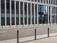 the empty street near buildings has a lot of glass windows and fencing on both sides