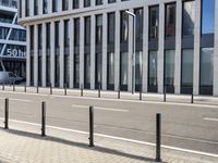 the empty street near buildings has a lot of glass windows and fencing on both sides