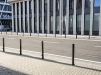 the empty street near buildings has a lot of glass windows and fencing on both sides