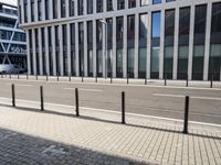 the empty street near buildings has a lot of glass windows and fencing on both sides