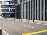 the empty street near buildings has a lot of glass windows and fencing on both sides