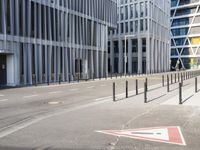 the empty street near buildings has a lot of glass windows and fencing on both sides