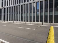 the empty street near buildings has a lot of glass windows and fencing on both sides