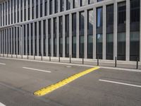 the empty street near buildings has a lot of glass windows and fencing on both sides