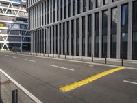 the empty street near buildings has a lot of glass windows and fencing on both sides