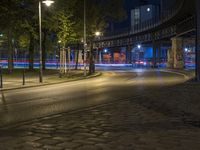 a very empty street at night with some cars driving by and a bridge in the background