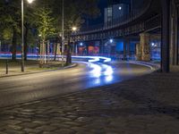 a very empty street at night with some cars driving by and a bridge in the background