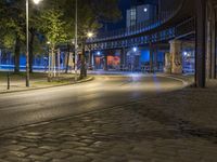 a very empty street at night with some cars driving by and a bridge in the background