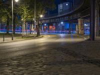 a very empty street at night with some cars driving by and a bridge in the background