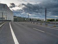 an empty street that runs along side of a high rise building with an industrial looking structure in the distance