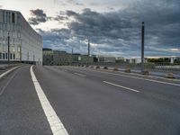 an empty street that runs along side of a high rise building with an industrial looking structure in the distance