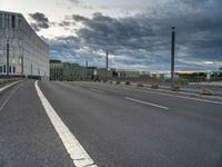 an empty street that runs along side of a high rise building with an industrial looking structure in the distance