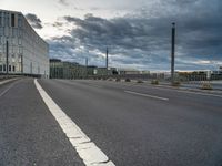 an empty street that runs along side of a high rise building with an industrial looking structure in the distance