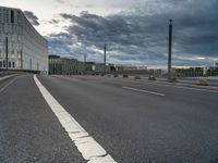 an empty street that runs along side of a high rise building with an industrial looking structure in the distance