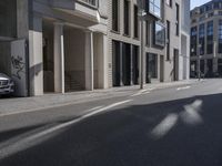the shadows of cars are on the empty street on the sidewalk and a building is in the distance