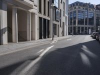 the shadows of cars are on the empty street on the sidewalk and a building is in the distance