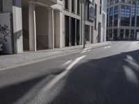 the shadows of cars are on the empty street on the sidewalk and a building is in the distance