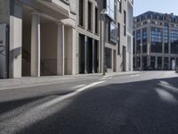 the shadows of cars are on the empty street on the sidewalk and a building is in the distance