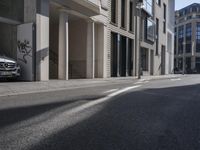 the shadows of cars are on the empty street on the sidewalk and a building is in the distance