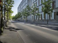 a empty street next to a building with tall windows on the side of it is lined with trees