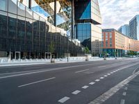 empty street next to tall glass building in urban area, with city buildings in background