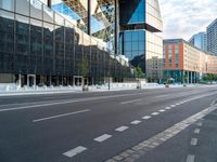 empty street next to tall glass building in urban area, with city buildings in background