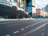 empty street next to tall glass building in urban area, with city buildings in background