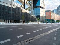 empty street next to tall glass building in urban area, with city buildings in background