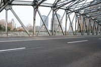 an empty street with a bridge with a street in the background with skyscrapers behind it