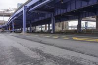 the empty street is lined with traffic and blue supports, near the brooklyn bridge bridge