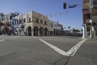 an empty street has cars and buildings in the background, with a stop light on each side of the road