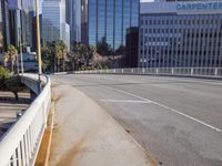 the street is empty in a big city with tall buildings behind it and a pedestrian walking across