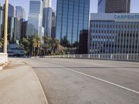 the street is empty in a big city with tall buildings behind it and a pedestrian walking across